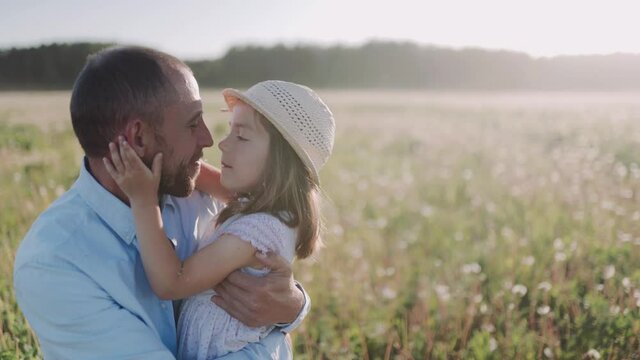 Father and daughter playing, touch the nose of each other on the field during sunset. A caucasian man and his daughter hug each other. Happy family Father's day.