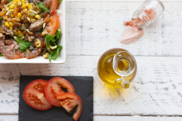 overhead view of a rustic white table with a salad with chia and lamb's lettuce, cut tomato oil and himalayan salt