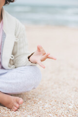 Young caucasian girl meditate at the beach, doing yoga lotus pose, child meditation outdoors