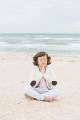 Fototapeta na wymiar Young caucasian girl meditate at the beach, doing yoga lotus pose, child meditation outdoors