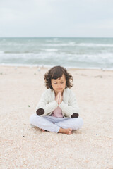 Fototapeta na wymiar Young caucasian girl meditate at the beach, doing yoga lotus pose, child meditation outdoors