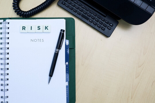 Text on risk on block letters, notebook, pen, and telephone on wooden desk