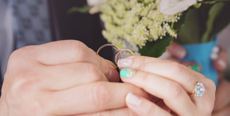 Hands of newlyweds holding gold wedding rings close-up. The bride has a Beautiful mint-colored...