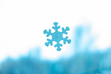 Blue paper snowflake on glass, a symbol of winter, New Year's decor, photography.
