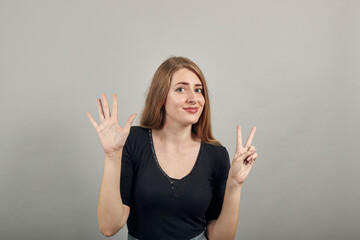 Showing 7 fingers hand gesture, show the number three with hands, pointing up arm while smiling confident, happy. young attractive woman, dressed black t-shirt, grey background