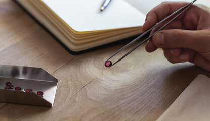 Hand holding a ruby gemstone with jewelry forceps. Gemologist workspace.