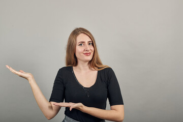 Shows direction of hands, demonstrates your product, represents an imaginary output, blank targeting, folded arm bent arrow. Young attractive woman, dressed black t-shirt, grey background