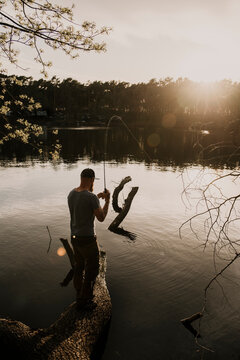 Rear view of man fishing in lake while standing on tree trunk