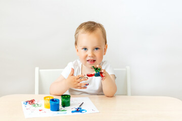 child boy 2 years old sitting at a table on a white isolated background and paints, early development, place for text