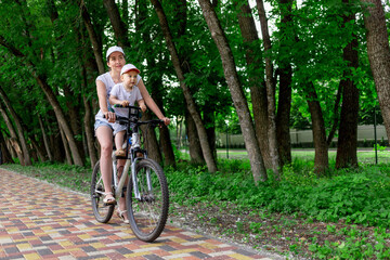 Naklejka premium mother and son ride a Bicycle, mother carries a child in a child's chair on a Bicycle in the Park in the summer