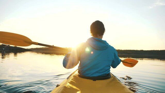 outdoor activities, man is kayaking on calm lake against backdrop of sunset rays