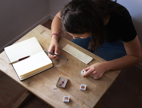 Female gemologist working observing precious stones in her workspace. Wooden table with notebook, suede, shovel and gems