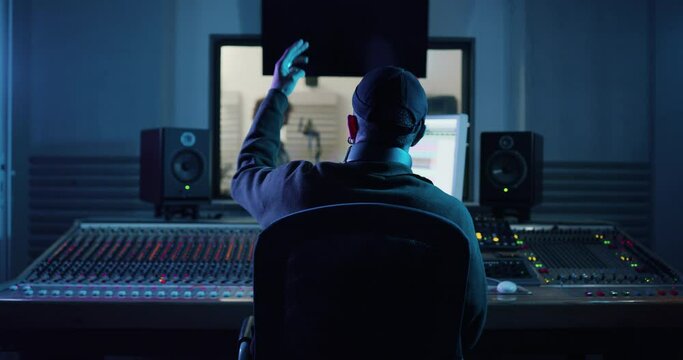 Back view of professional male sound producer with headphones is recording a new song with young african female singer in a music studio with colorful lights.