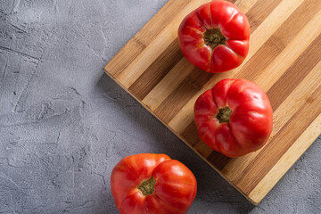 Three pink heirloom tomato vegetables, fresh red ripe tomatoes on wooden cutting board, vegan food, stone concrete background, top view