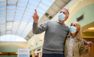 Senior couple shopping in a mall at coronavirus times, wearing masks