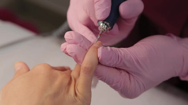 Manicurist cuts nails with a machine to a client in a manicure salon.