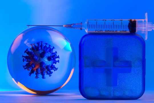 Mockup of virus in a glass sphere, medical injection syringe with medicine or vaccine from COVID -19 and a pill case on blue background.