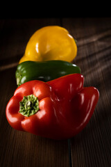 Red, green and yellow bell peppers, lit on a wooden table.