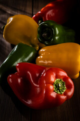 Red, green and yellow bell peppers, lit on a wooden table.