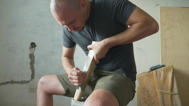 bald man planes a planer wooden bar sitting indoors