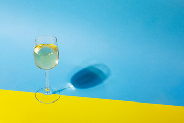 Glass of white wine on yellow blue background with long shadow. Shadow effect, hard light. Copy...
