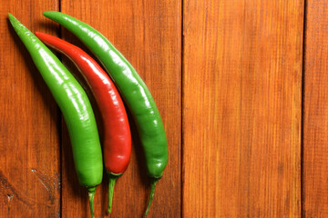 Two green and one red chili pepper pods lie on the left on a wooden brown table