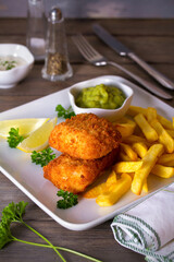 Fish and chips, mushy peas and sauce on white plate. Vertical image