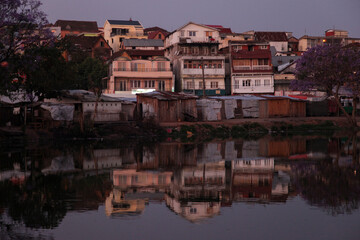 Obraz premium Houses and buildings reflect in the still waters of a lake in Antananarivo, Madagascar just after sunset.