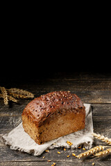 Loaf of black bread with seeds on textile towel on rustic wooden texture background. Vertical composition with copy space