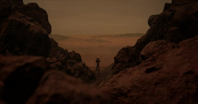 DOLLY IN Back view of lonely astronaut walking on a surface of a red rocky planet. Mars colonization concept. Dust effect added