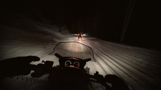 Person riding while following friends on snowmobile over snow in dark at night - Whistler, British Columbia