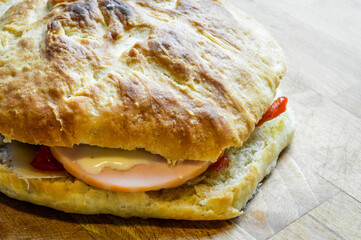 Little italian focaccia bread stuffed with turkey ham, red bell peppers, cheese and red onions on wooden cutting board, close up.

