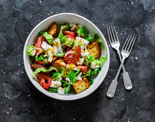 Simple rustic italian salad with fresh tomatoes, ciabatta crunchy bread, mozzarella cheese, green salad  on a dark background, top view