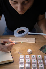 Geologist woman working at her desk looking at a precious stone in a lamp. Workspace with jewelry tools.