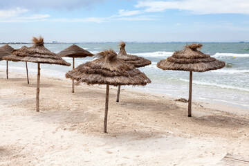 Empty sandy beach at stormy weather, sun umbrellas from palm leaf are on sand