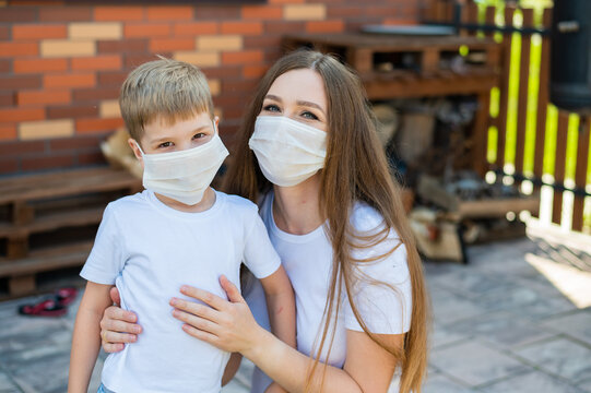 Woman hugs her son in a mask outdoors. Happy little boy with mother are walking in the backyard during isolation. Protection against the spread of coronavirus. Flu outbreak.