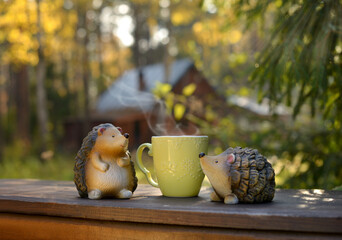 Healthy herbal tea. Beautiful coffee cup with steam, nature background and warm light. Yellow Cup of coffee on an autumn background. Two ceramic hedgehogs. Figures of two hedgehogs. © Artemida
