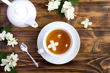Jasmine green tea in the white cup, teapot and flowers on the brown wooden background. Top view....