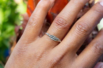 Hand wearing metal decorative ring in the shape of feather, touching beautiful plant