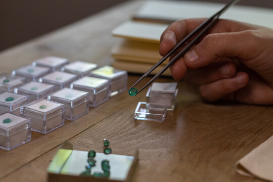 Hand holding a emerald gemstone with jewelry forceps. Gemologist workspace.