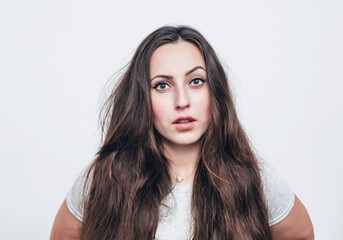 Portrait of a girl with long dark hair on a white background looking at the camera. Light surprise.