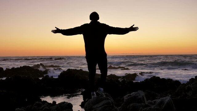 Young men warrior monk practicing silhouette tai chi karate kung Fu on the rocky stones horizon at sunset or sunrise. Art of self-defense. Silhouette on a background of dramatic epic waves