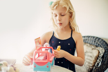 Cute little girl playing toy car bus with doll. Active little child kid playing alone on a quarantine at home. Happy authentic real childhood lifestyle.