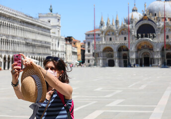 tourist wearing a surgical mask takes a picture in Venice during