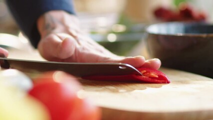 Close-up shot of hands of male cook cutting red hot pepper on wooden board and removing pulp with knife