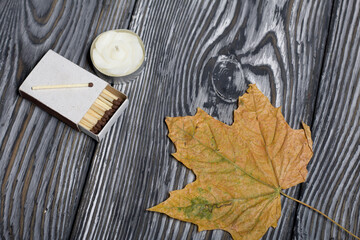 Autumn maple leaves are yellow. Decorative candle with matches. On pine boards painted black and white.