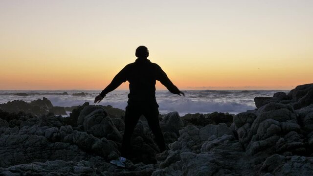 Young men warrior monk practicing silhouette tai chi karate kung Fu on the rocky stones horizon at sunset or sunrise. Art of self-defense. Silhouette on a background of dramatic epic waves