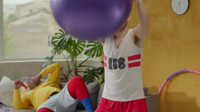 Expressive retro fitness guy doing fake training exercises with fit ball. Lazy afro-american chubby man relaxing on sofa instead of workout. Comedy. Fun.