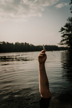 Woman's hand holding cigarette while swimming in lake