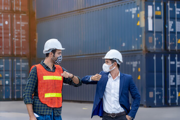 New normal concept,Engineer worker greeted by bumping elbow for distance between people wearing mask and helmet in the factory or container yard Prevent accident from work or dust and Coronavirus.